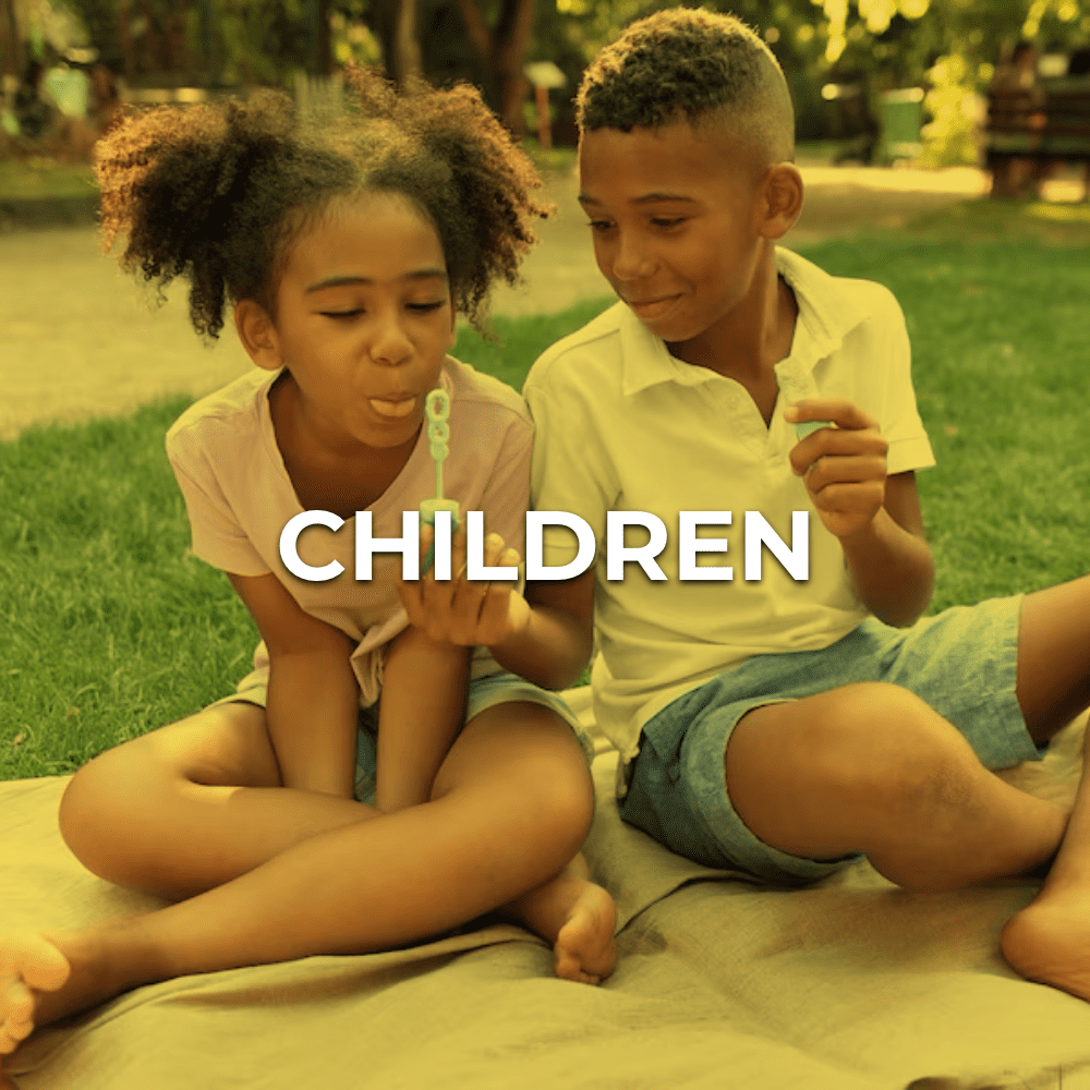 Two children sitting on a blanket in the grass.