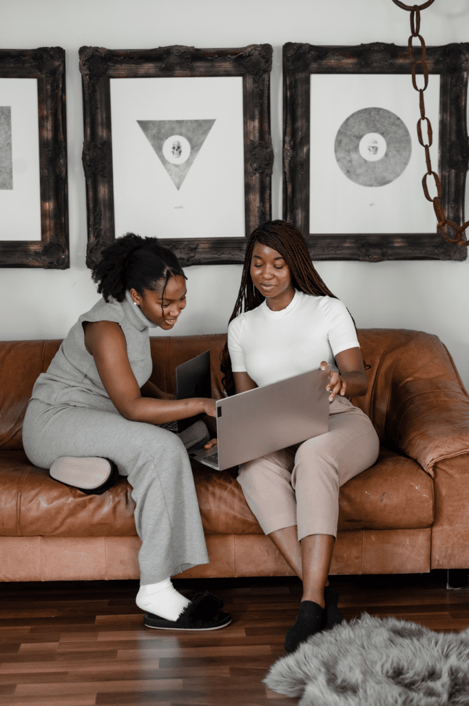 Two women sitting on a couch looking at a laptop.