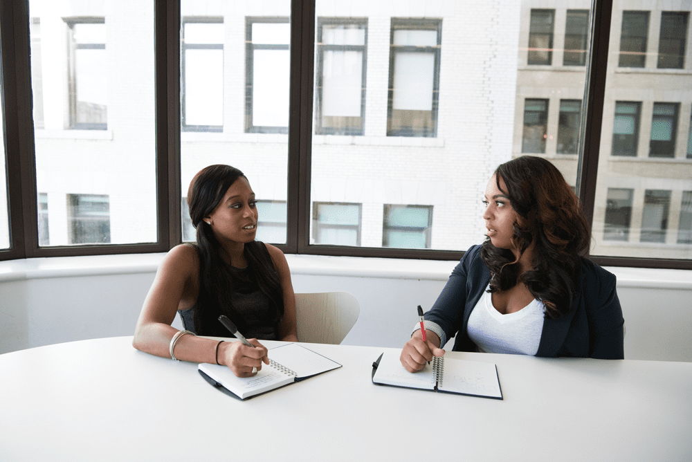 Two women sitting at a table with papers and pens.