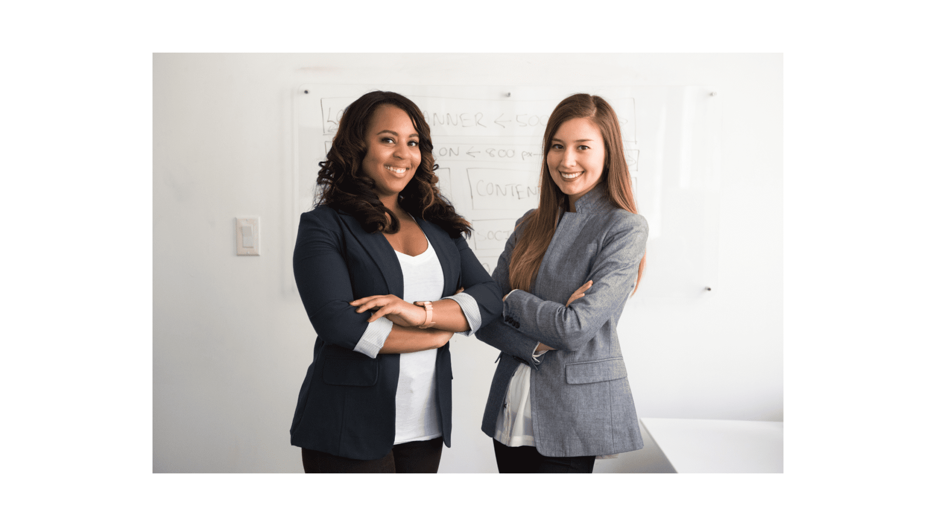 Two women standing next to each other in front of a white wall.